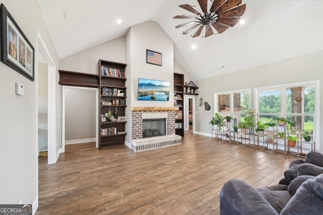living area with ceiling fan, a fireplace, high vaulted ceiling, baseboards, and wood finished floors