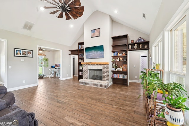 living area featuring visible vents, a brick fireplace, wood finished floors, baseboards, and high vaulted ceiling