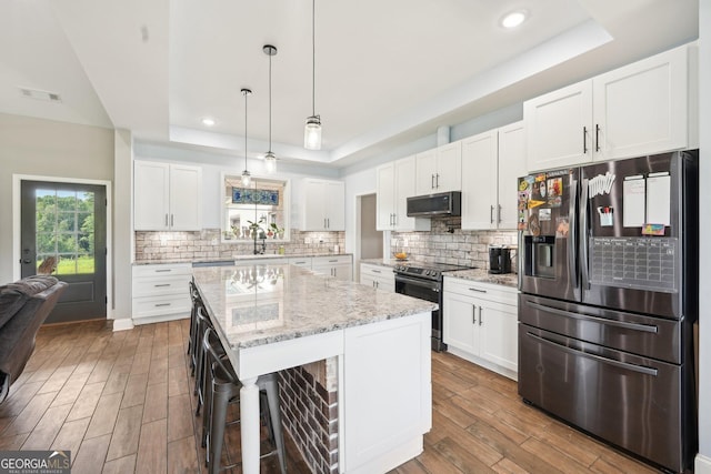 kitchen featuring a tray ceiling, stainless steel appliances, wood finished floors, and a sink