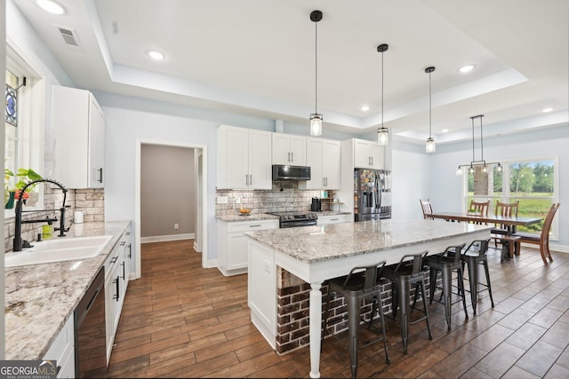 kitchen featuring visible vents, a raised ceiling, a sink, backsplash, and stainless steel appliances