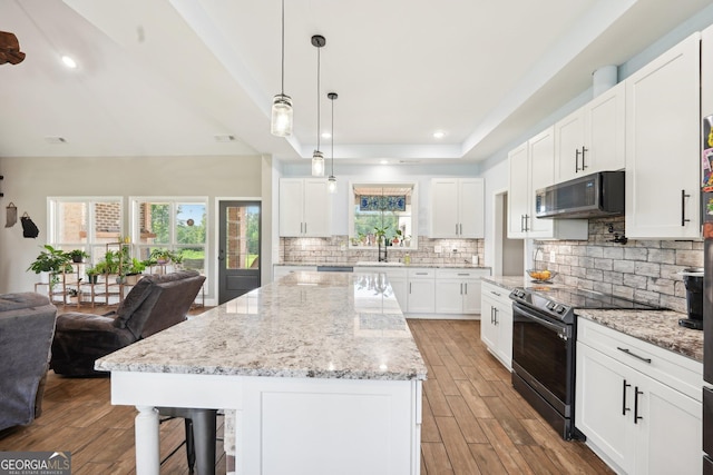 kitchen featuring tasteful backsplash, stainless steel range with electric stovetop, white cabinetry, wood finished floors, and a kitchen bar