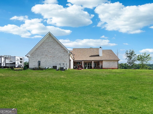 rear view of house with central air condition unit, a yard, and a chimney