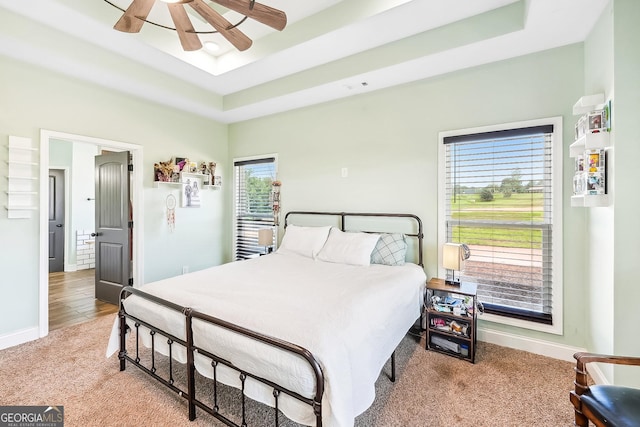 carpeted bedroom featuring baseboards, ceiling fan, and a raised ceiling
