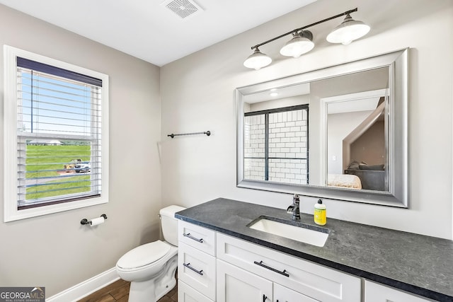 bathroom with vanity, toilet, baseboards, wood finished floors, and visible vents