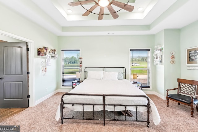 bedroom with carpet floors, a tray ceiling, and multiple windows