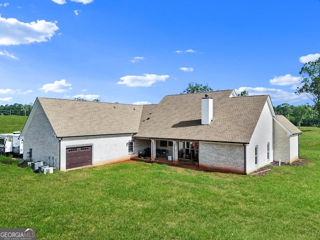 back of property featuring central AC, a chimney, a shingled roof, an attached garage, and a yard