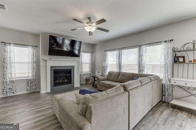 living area with a fireplace with flush hearth, light wood-style floors, a ceiling fan, and baseboards