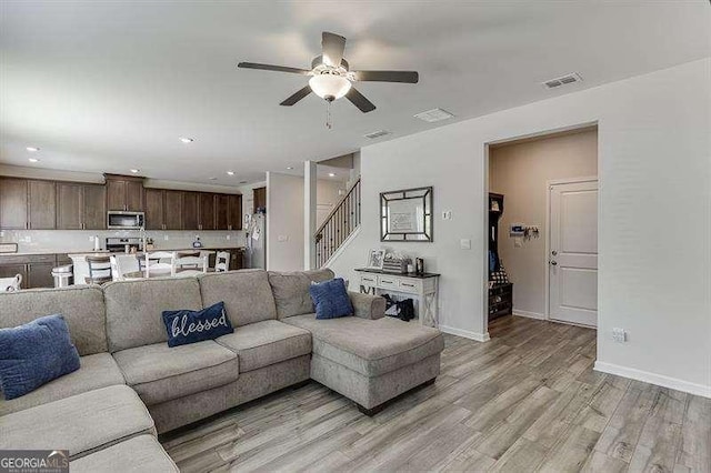 living area featuring stairs, ceiling fan, light wood-style flooring, baseboards, and recessed lighting