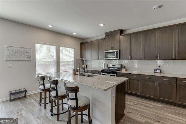 kitchen featuring stainless steel appliances, backsplash, a sink, light wood-type flooring, and a breakfast bar area