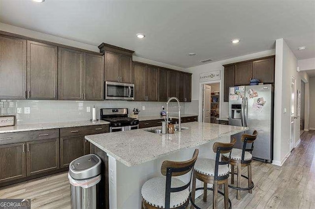 kitchen featuring dark brown cabinets, a sink, decorative backsplash, stainless steel appliances, and light stone countertops