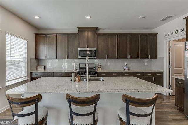 kitchen featuring dark brown cabinets, an island with sink, stainless steel appliances, visible vents, and dark wood-style floors