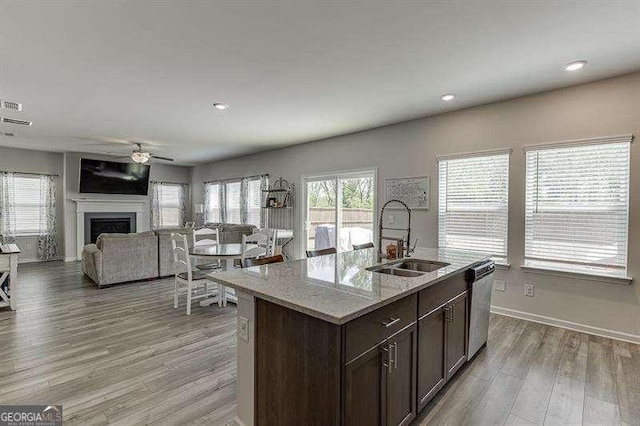 kitchen featuring a sink, light wood-type flooring, ceiling fan, dishwasher, and a fireplace