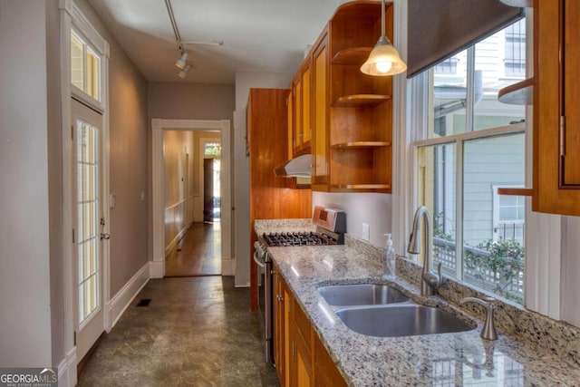kitchen with a sink, brown cabinets, gas range, a healthy amount of sunlight, and under cabinet range hood