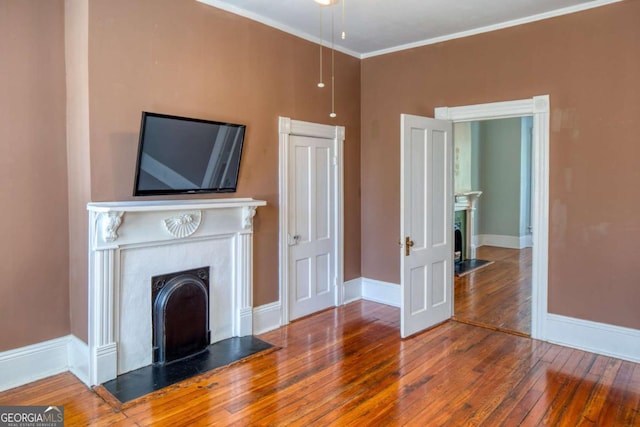 unfurnished living room with a fireplace, wood-type flooring, crown molding, and baseboards