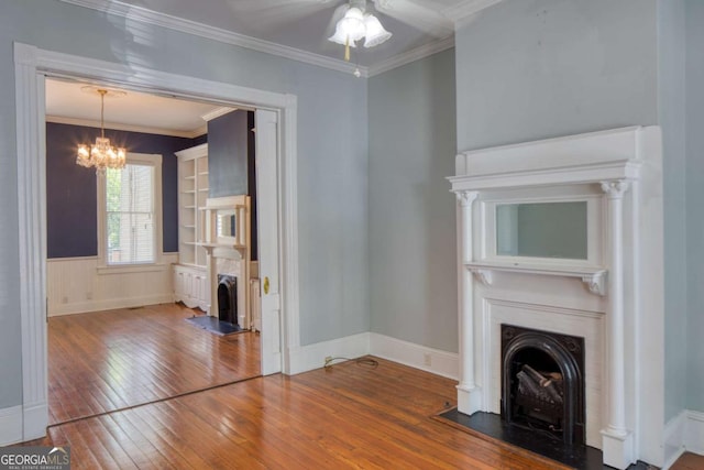 unfurnished living room with a fireplace with flush hearth, a wainscoted wall, ceiling fan with notable chandelier, crown molding, and hardwood / wood-style flooring