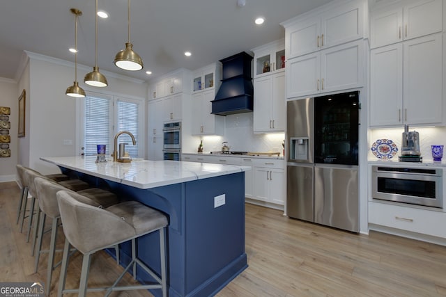 kitchen featuring appliances with stainless steel finishes, custom range hood, ornamental molding, light wood finished floors, and white cabinets