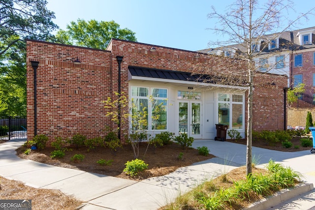 view of front of property with french doors, brick siding, fence, and a standing seam roof