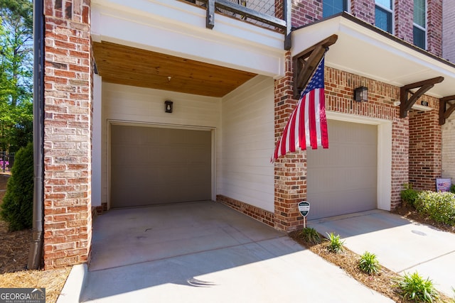 entrance to property featuring brick siding, driveway, a balcony, and an attached garage