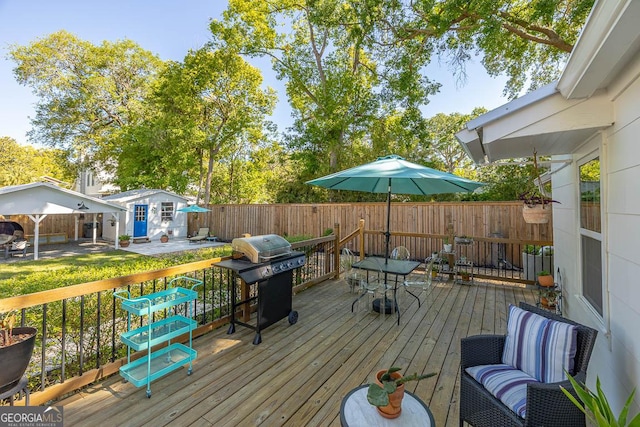 wooden terrace featuring a grill, fence, an outbuilding, and outdoor dining space