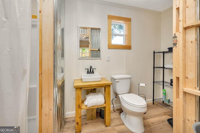 full bathroom featuring a shower with curtain, a sink, toilet, wood finished floors, and ornamental molding
