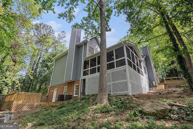 rear view of property with a chimney, brick siding, a sunroom, central AC unit, and a deck