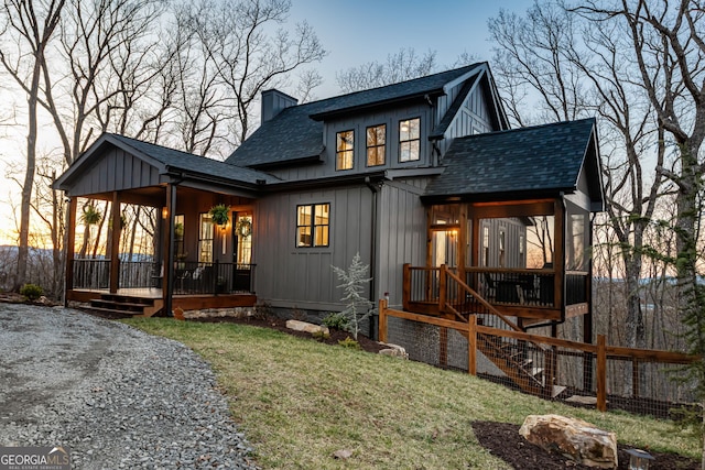 back of house featuring a chimney, covered porch, a lawn, a shingled roof, and board and batten siding