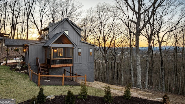 back of house at dusk with board and batten siding, roof with shingles, and a lawn