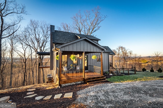 view of front facade with a chimney, a front lawn, board and batten siding, a porch, and roof with shingles
