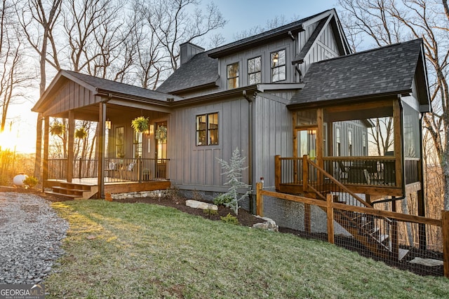 rear view of property with a lawn, a shingled roof, a chimney, and covered porch