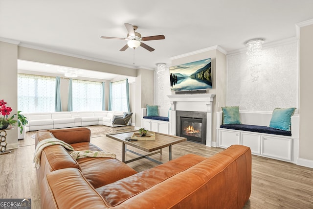 living room with ceiling fan, crown molding, a glass covered fireplace, and light wood finished floors