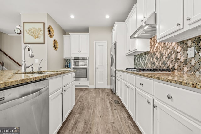 kitchen featuring under cabinet range hood, stainless steel appliances, a sink, light wood-type flooring, and white cabinetry