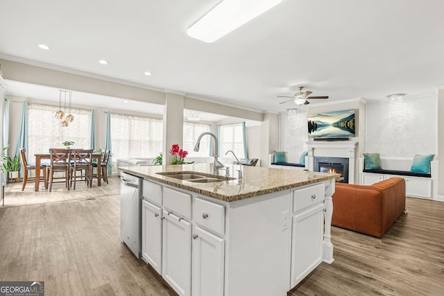 kitchen featuring stainless steel dishwasher, a sink, crown molding, a glass covered fireplace, and ceiling fan