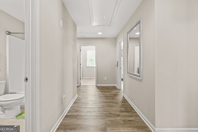 corridor featuring attic access, wood finished floors, baseboards, and recessed lighting
