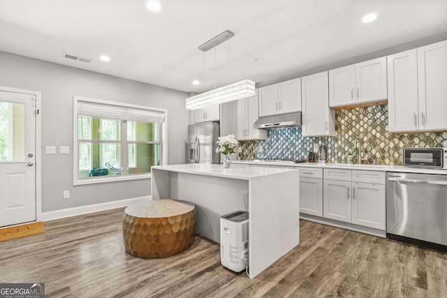 kitchen with a sink, under cabinet range hood, stainless steel appliances, dark wood-style flooring, and visible vents