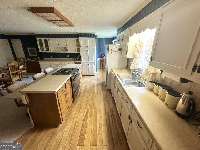 kitchen featuring a textured ceiling, a sink, light wood finished floors, light countertops, and gas stove