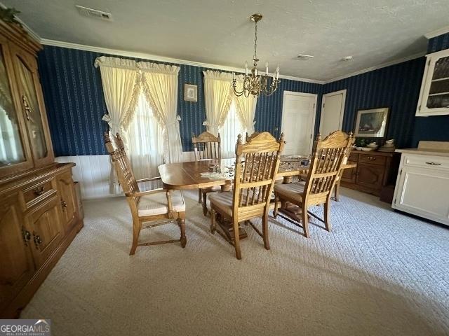 dining space with light carpet, ornamental molding, a chandelier, and wallpapered walls