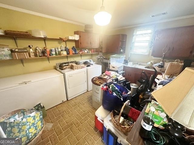 washroom featuring brick floor, washer and dryer, ornamental molding, and laundry area