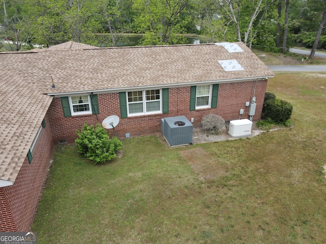rear view of property featuring central AC unit, crawl space, a shingled roof, a yard, and brick siding