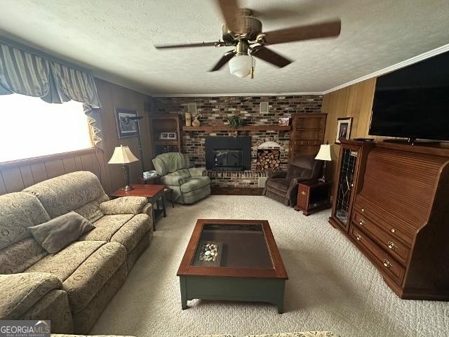 carpeted living room with a textured ceiling, wooden walls, ceiling fan, ornamental molding, and a brick fireplace