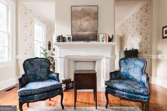 living area featuring wood finished floors, ornamental molding, wallpapered walls, a fireplace, and baseboards