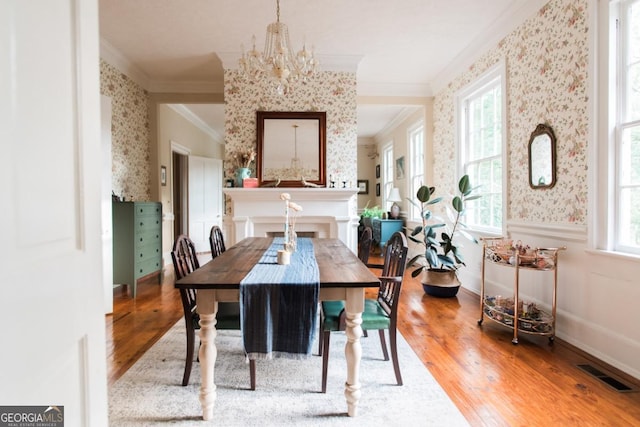 dining space featuring wallpapered walls, crown molding, healthy amount of natural light, a chandelier, and wood finished floors