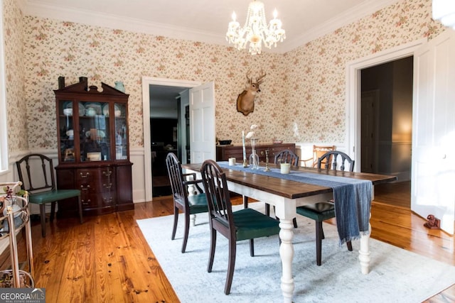 dining area featuring a chandelier, crown molding, light wood-style flooring, wainscoting, and wallpapered walls