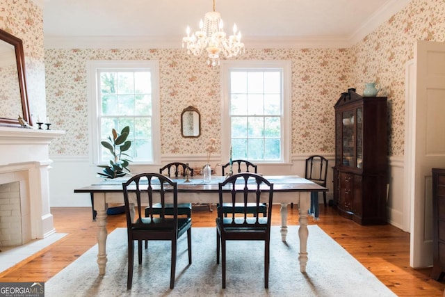 dining space with wainscoting, wood finished floors, ornamental molding, wallpapered walls, and a chandelier