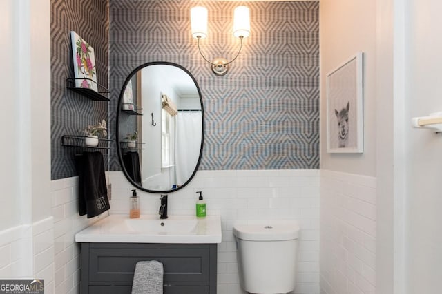 bathroom featuring tile walls, toilet, a wainscoted wall, vanity, and wallpapered walls