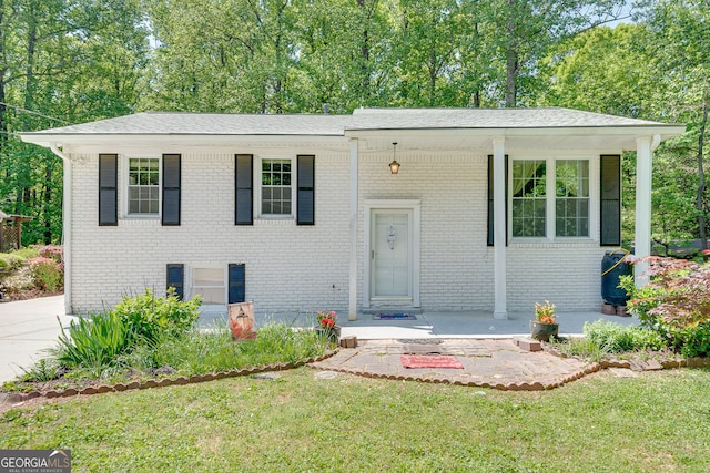 view of front of home with covered porch, brick siding, a front yard, and view of wooded area