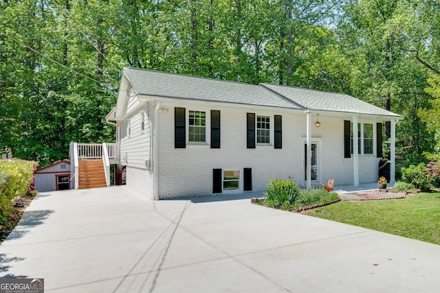 bi-level home featuring a porch, brick siding, concrete driveway, an outbuilding, and view of wooded area