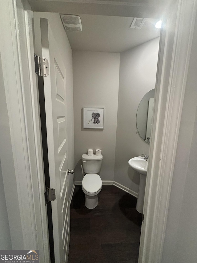 half bathroom with baseboards, wood finished floors, and toilet