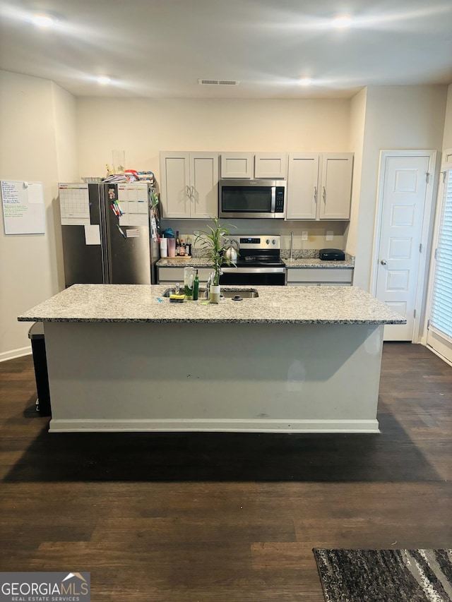kitchen with appliances with stainless steel finishes, light stone countertops, a kitchen island with sink, a kitchen bar, and dark wood-style flooring