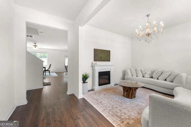 living room featuring dark wood-style floors, visible vents, baseboards, a glass covered fireplace, and ceiling fan with notable chandelier
