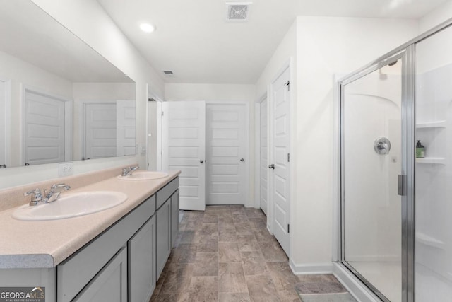 bathroom with stone finish flooring, a sink, double vanity, and a stall shower
